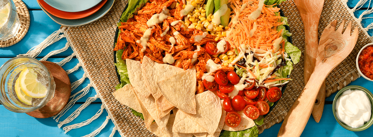 Overhead shot of al pastor taco salad with crispy tortilla chips and bowls of sour cream and salsa to the side