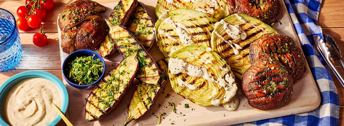 Overhead shot of grilled cabbage, egg plant, and mushroom on a cutting board topped with yogurt-mint sauce.