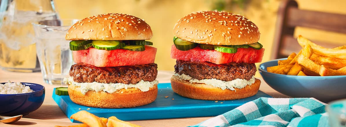 Two beef burgers with watermelon slices in between a bun, and side of fries.